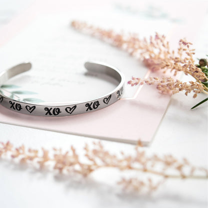 Inspirational stainless steel cuff bracelet with repeating XO's and hearts on the outside and engraved words 'My maid of honor today, my sister forever' on the inside. Adjustable and hypoallergenic, perfect as a thoughtful gift for sisters and symbolizing the bond of sisterhood.