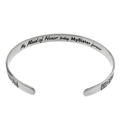 Inspirational stainless steel cuff bracelet with an elegant Victorian flower design on the outside and engraved words 'My maid of honor today, my sister forever' on the inside. Adjustable and hypoallergenic, perfect as a thoughtful gift for sisters and symbolizing the enduring bond of sisterhood.